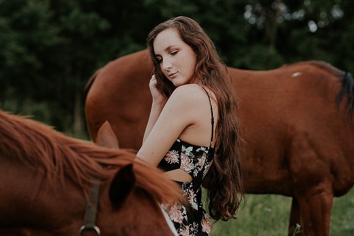 Frau in Sommerkleid steht zwischen zwei Pferden auf der Weide.