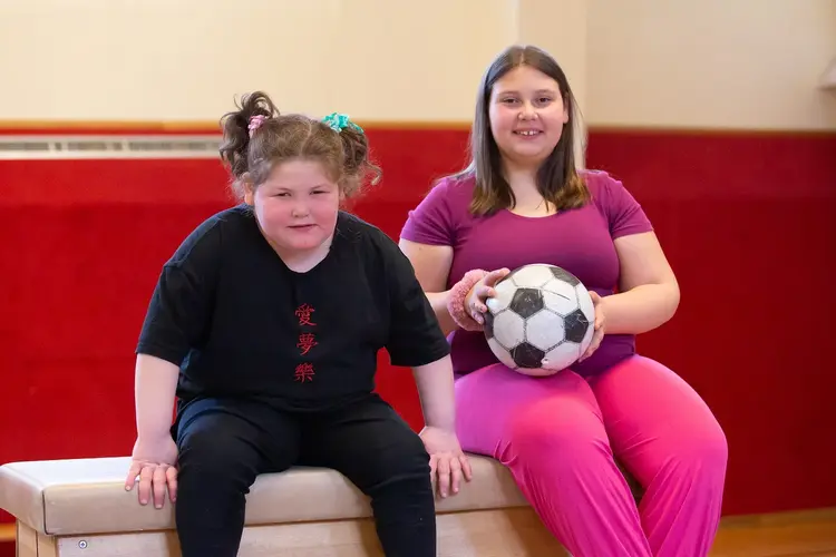 Lachende, übergewichtige Kindern sitzen auf einem Bock im Turnsaal.