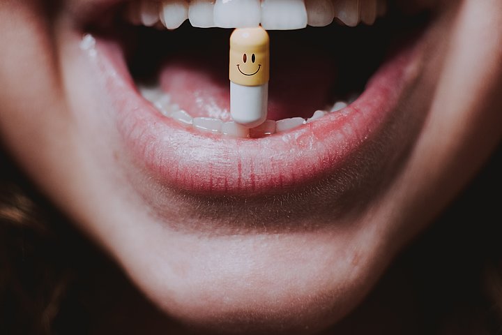 Frau hat Tablette mit lächelndem Gesicht zwischen ihren Zähnen.
